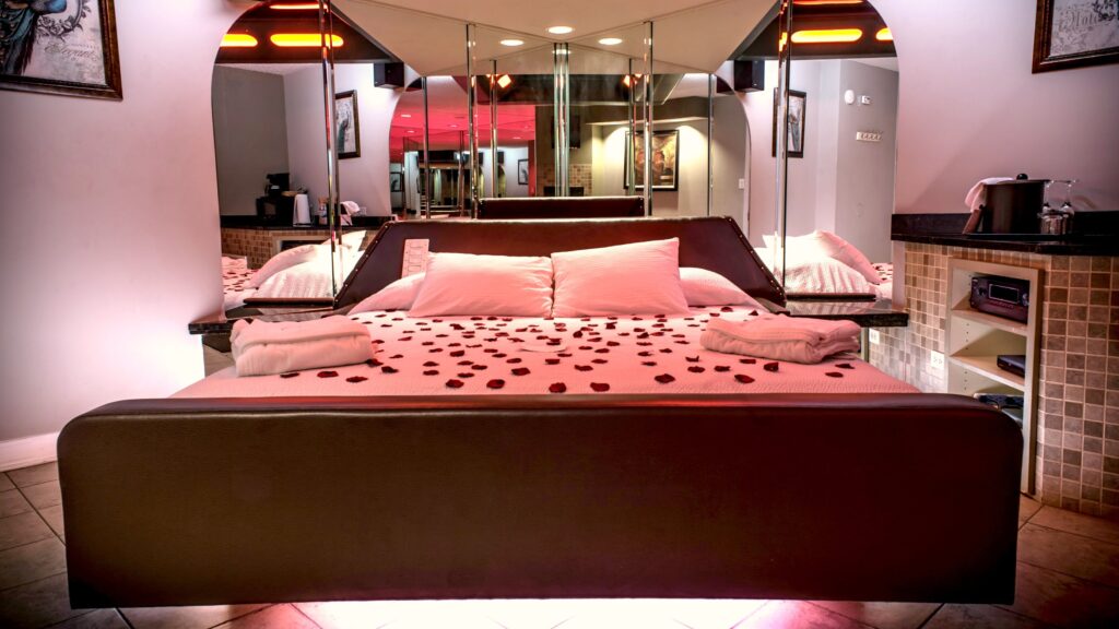 Romantic hotel suite with mirrored walls, decorative lighting, and a large bed prepared for couples