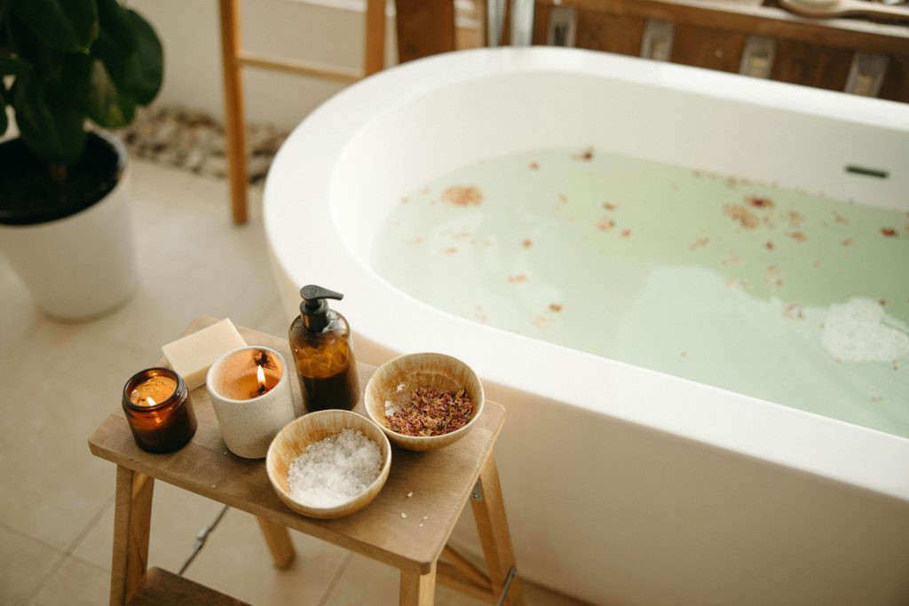 Relaxing bath setup with freestanding tub, bath salts, candles, and spa accessories in a calm bathroom