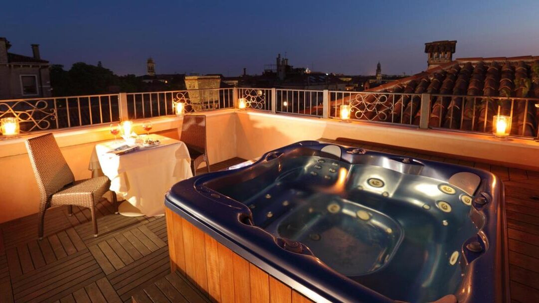 Private rooftop terrace with outdoor hot tub, candlelit dining table, and city skyline view at night