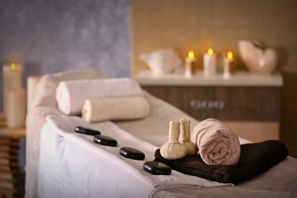 Spa massage table with rolled towels, hot stones, and soft candlelight in a quiet wellness room