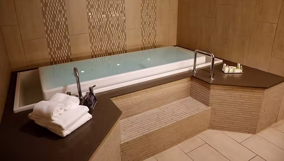 Oasis Hotel & Conv. Center, Ascend Hotel Collection Built-in spa tub with tiled surround, steps, and folded towels inside a private indoor spa area