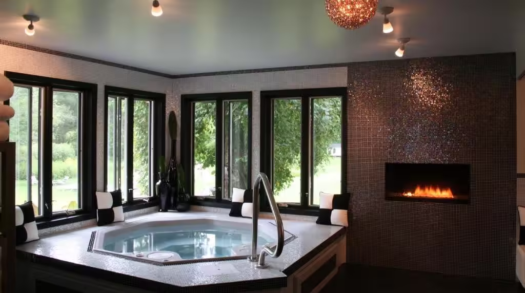 The Roxbury Indoor hot tub set into a tiled platform with seating, large windows, and a lit fireplace nearby