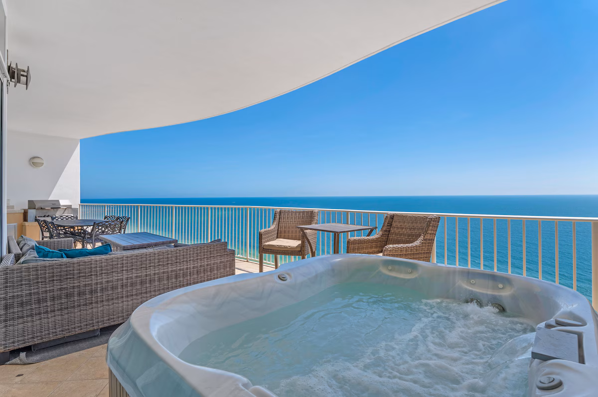 Private balcony hot tub with wide coastal views at sunset next to a modern suite.